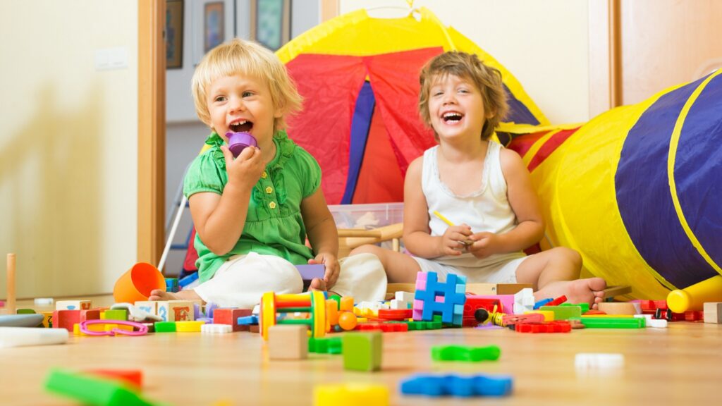 Two cheerful little girls playing with blocks in home interior